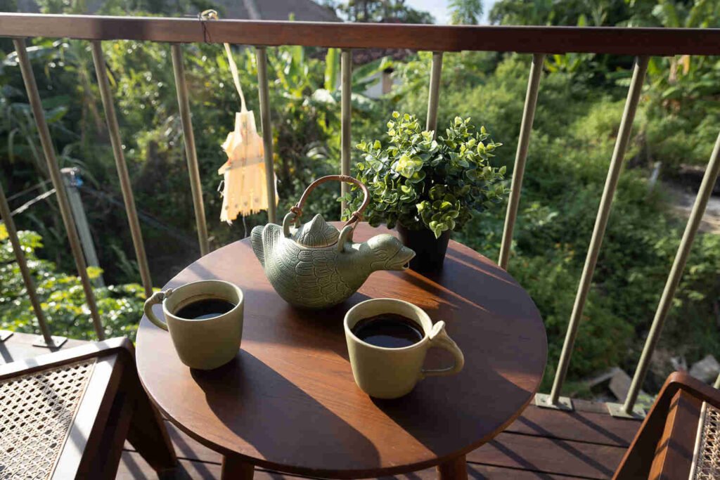 Green ceramic teapot and two mugs of coffee on the round balcony table at The Nest, with the jungle just beyond the railing