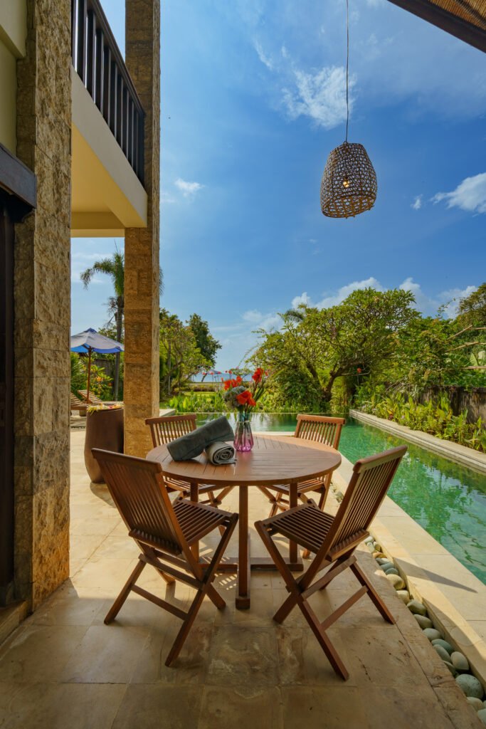 Woven rattan pendant lamp hanging against blue sky beside the sandstone balcony columns at Samastiti by the Beach in Lovina