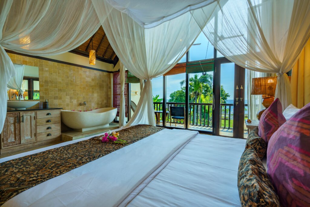 View from the master bed at Samastiti by the Beach in Lovina past a stone bathtub and timber vanity to balcony doors framing the sea