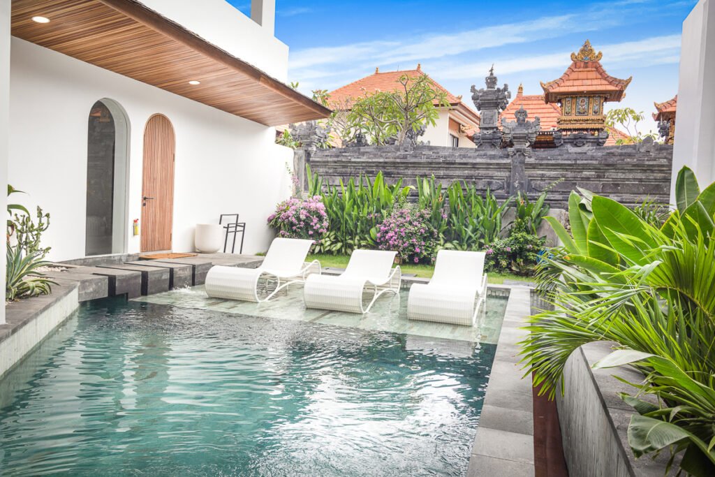 Private pool at the Pool Garden Suite with three loungers on the deck, an arched timber door into the villa and a Balinese temple next door