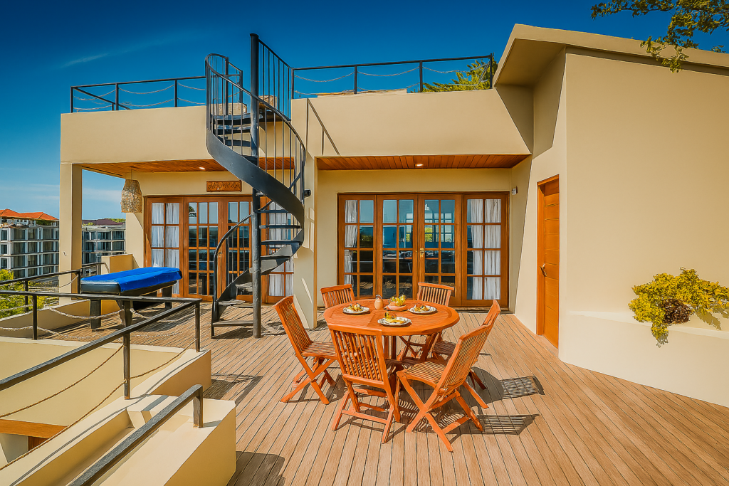 Terrace of the Seaview Penthouse with a round timber table set for breakfast, French doors into the apartment and a spiral staircase up to the roof deck