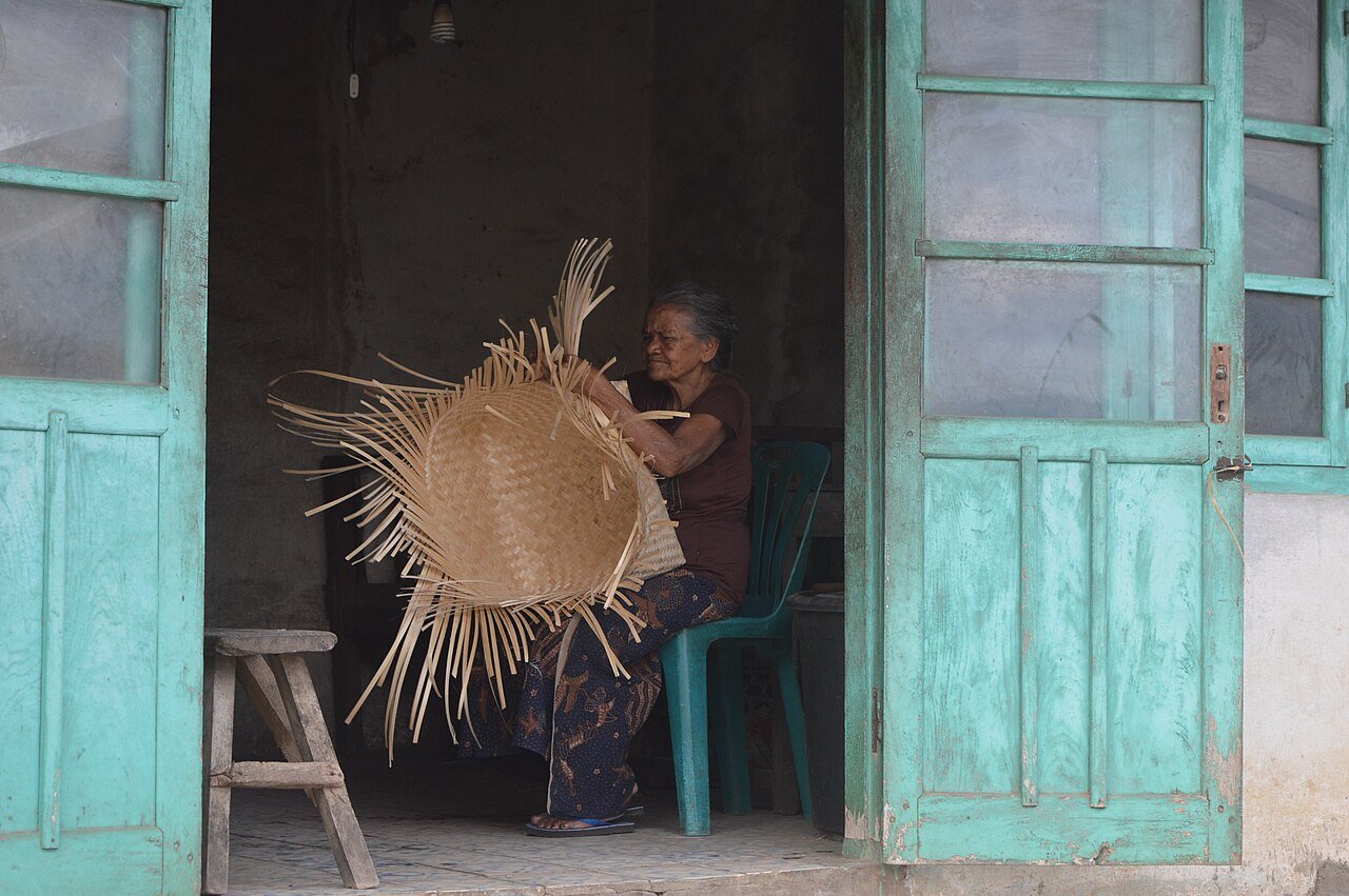 Village woman weaving a large bamboo basket in a doorway in Sidetapa, Bali
